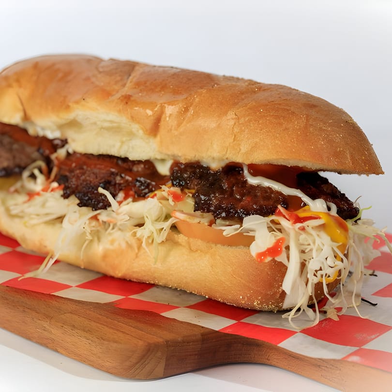 A Grumpy G burger on a long bun with shredded cabbage, tomatoes, and sauces.