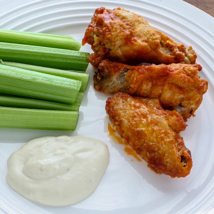 Grumpy G's buffalo wings with celery sticks and ranch dressing on a white plate.
