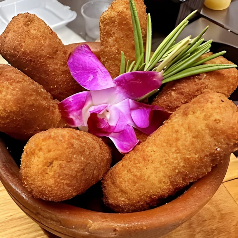 A bowl of golden-brown fried croquettes garnished with a vibrant purple orchid and green herbs.